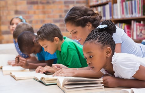 Cute pupils and teacher lying on floor in library at the elementary school