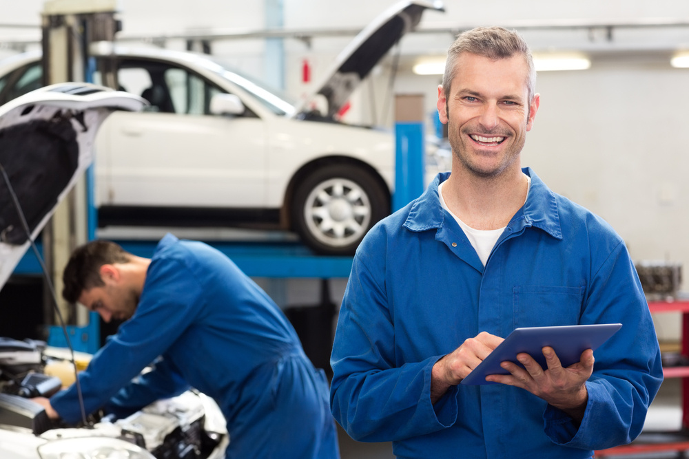 Smiling mechanic using a tablet pc at the repair garage